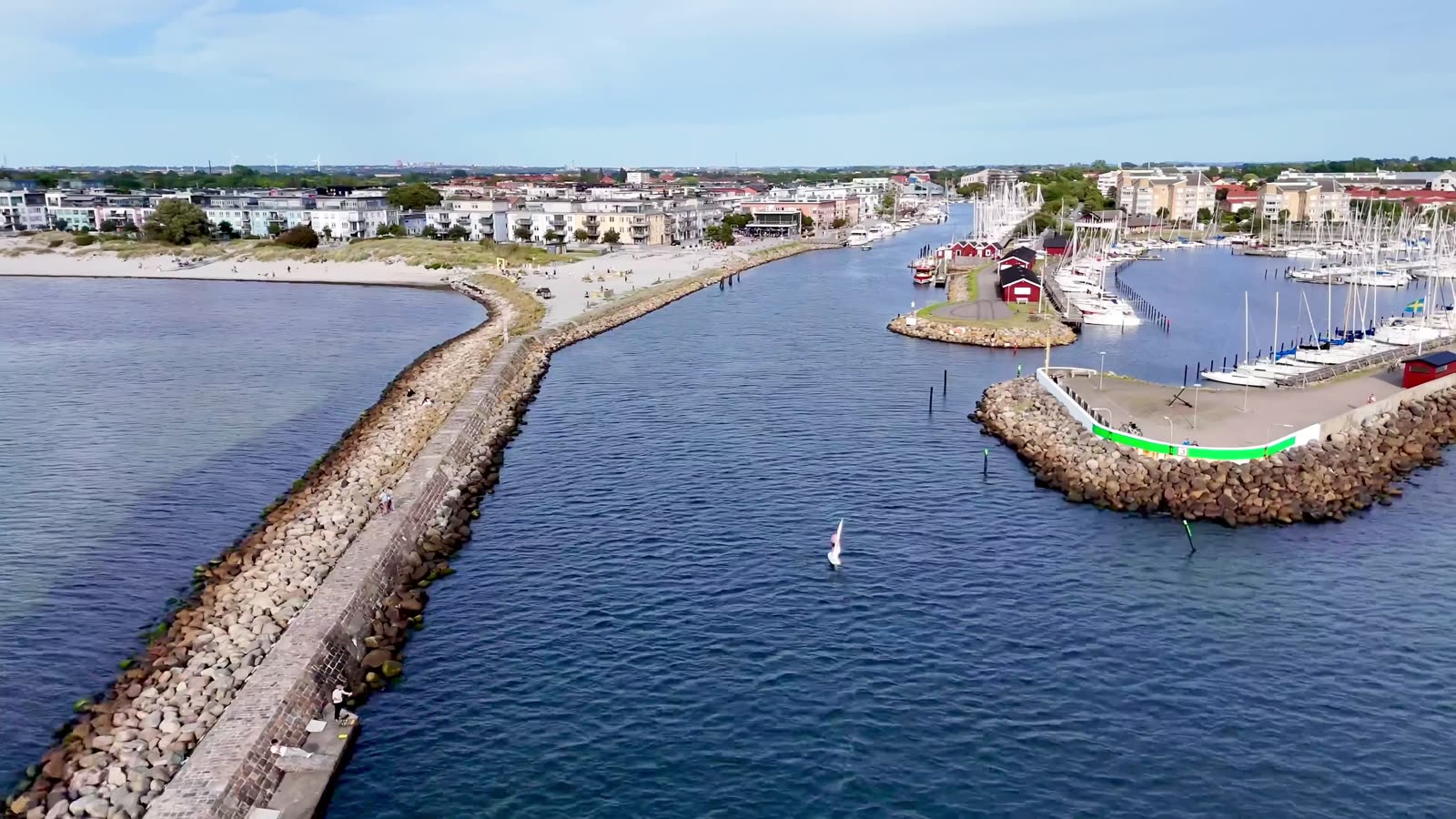 Drönarbild över Lomma hamn med stranden, piren och småbåtshamnen, med eFoil-föraren och flaggan i inloppet